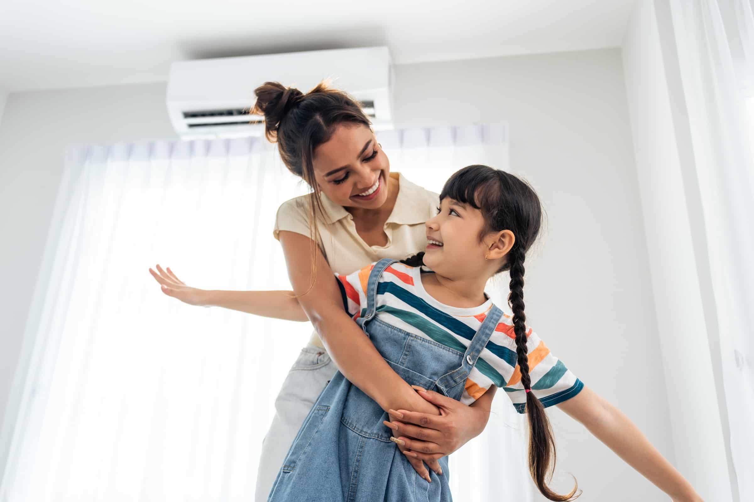 Mother playing with daughter in the living room with a heat pump on the wall in the background