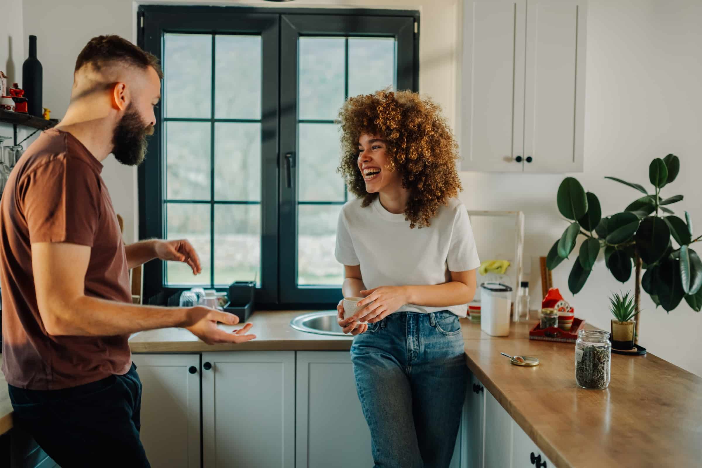 Young couple being playful and comfortable in the kitchen while it snows outside the window