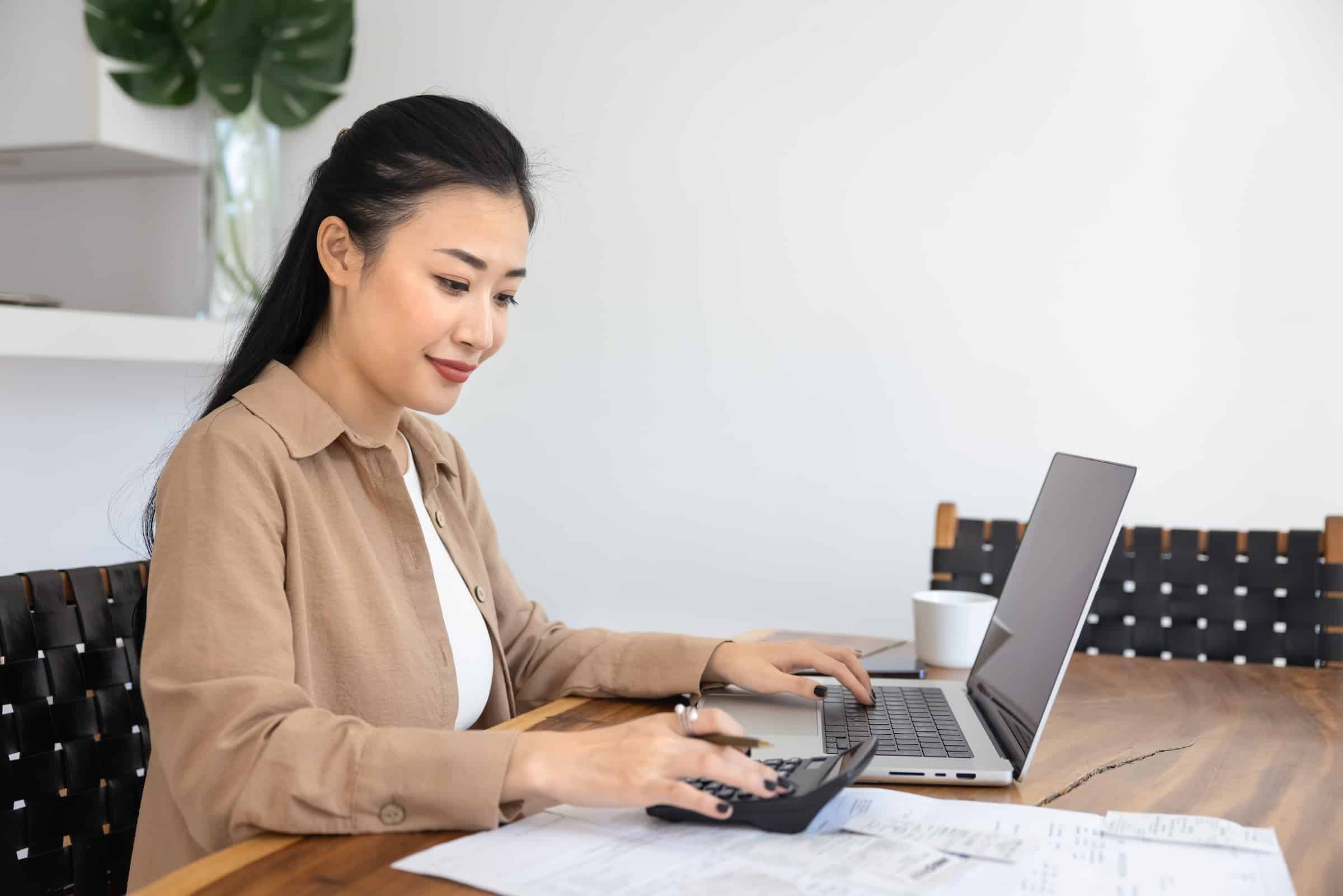 Woman using laptop and calculator to look up savings on heat pumps